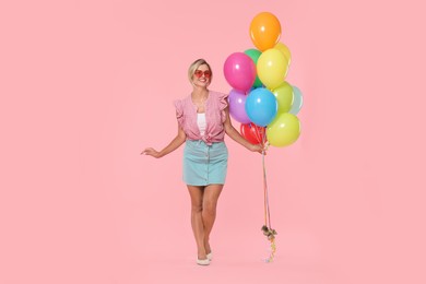 Photo of Smiling woman in sunglasses with bunch of colorful balloons on pink background