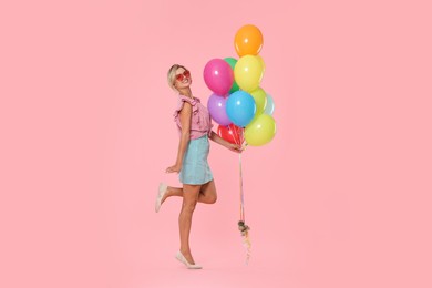 Photo of Smiling woman in sunglasses with bunch of colorful balloons on pink background