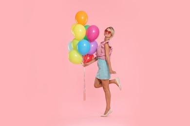 Photo of Smiling woman in sunglasses with bunch of colorful balloons on pink background