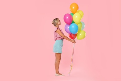 Photo of Smiling woman in sunglasses with bunch of colorful balloons on pink background