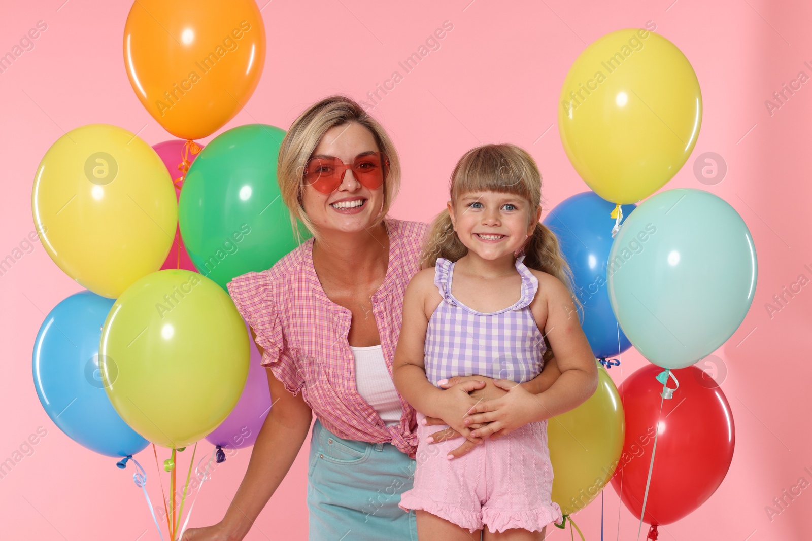 Happy mother in sunglasses and her little daughter with bunches of colorful balloons on pink background Photo of Happy mother in sunglasses and her little daughter with bunches of colorful balloons on pink background