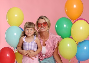 Photo of Happy mother in sunglasses and her little daughter with bunches of colorful balloons on pink background