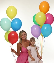 Photo of Happy mother in dress and her little daughter with bunches of colorful balloons on white background