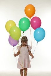 Photo of Happy little girl in dress with many colorful balloons on white background
