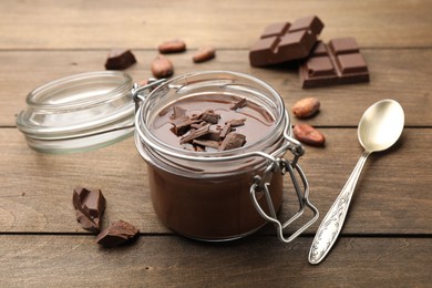 Photo of Delicious chocolate panna cotta in glass jar, nuts and spoon on wooden table, closeup