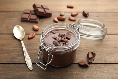 Photo of Delicious chocolate panna cotta in glass jar, nuts and spoon on wooden table, closeup