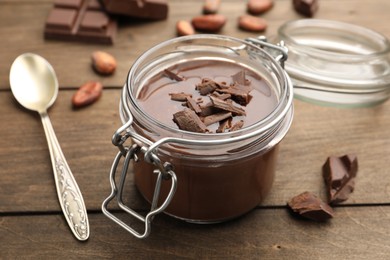 Photo of Delicious chocolate panna cotta in glass jar, nuts and spoon on wooden table, closeup