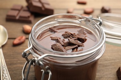 Photo of Delicious chocolate panna cotta in glass jar, nuts and spoon on wooden table, closeup