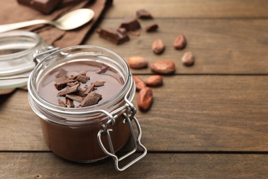 Photo of Delicious chocolate panna cotta in glass jar, nuts and spoon on wooden table, closeup. Space for text