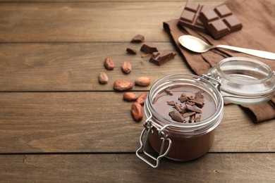 Photo of Delicious chocolate panna cotta in glass jar, nuts and spoon on wooden table, closeup. Space for text