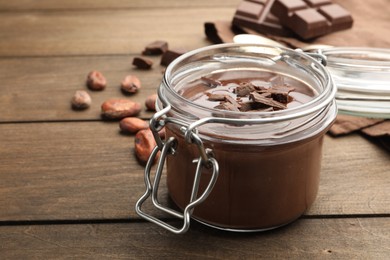 Photo of Delicious chocolate panna cotta in glass jar and nuts on wooden table, closeup. Space for text