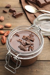 Photo of Delicious chocolate panna cotta in glass jar, nuts and spoon on wooden table, closeup