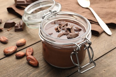 Photo of Delicious chocolate panna cotta in glass jar, nuts and spoon on wooden table, closeup