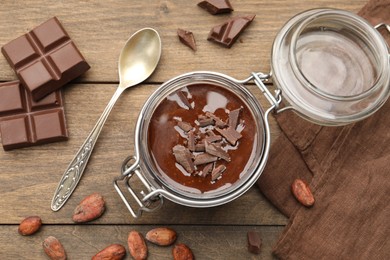 Photo of Delicious chocolate panna cotta in glass jar, nuts and spoon on wooden table, flat lay