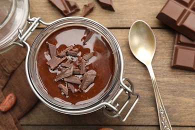 Photo of Delicious chocolate panna cotta in glass jar, nuts and spoon on wooden table, flat lay