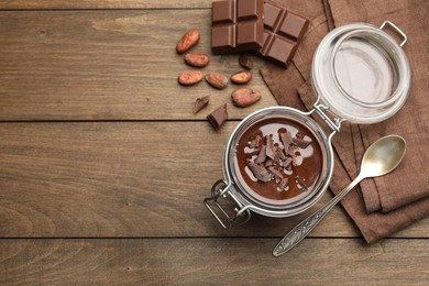 Photo of Delicious chocolate panna cotta in glass jar, nuts and spoon on wooden table, flat lay. Space for text
