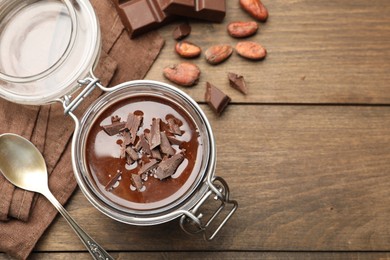 Photo of Delicious chocolate panna cotta in glass jar, nuts and spoon on wooden table, flat lay. Space for text