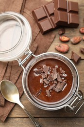 Photo of Delicious chocolate panna cotta in glass jar, nuts and spoon on wooden table, flat lay