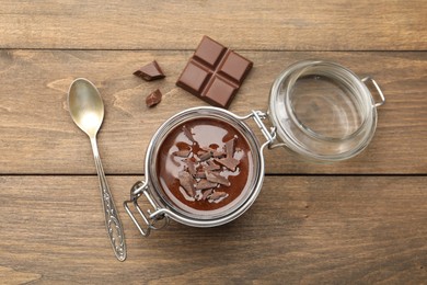 Photo of Delicious chocolate panna cotta in glass jar and spoon on wooden table, flat lay