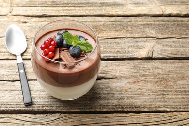 Photo of Delicious panna cotta with chocolate, berries, mint and spoon on wooden table, closeup. Space for text