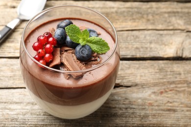 Photo of Delicious panna cotta with chocolate, berries, mint and spoon on wooden table, closeup. Space for text