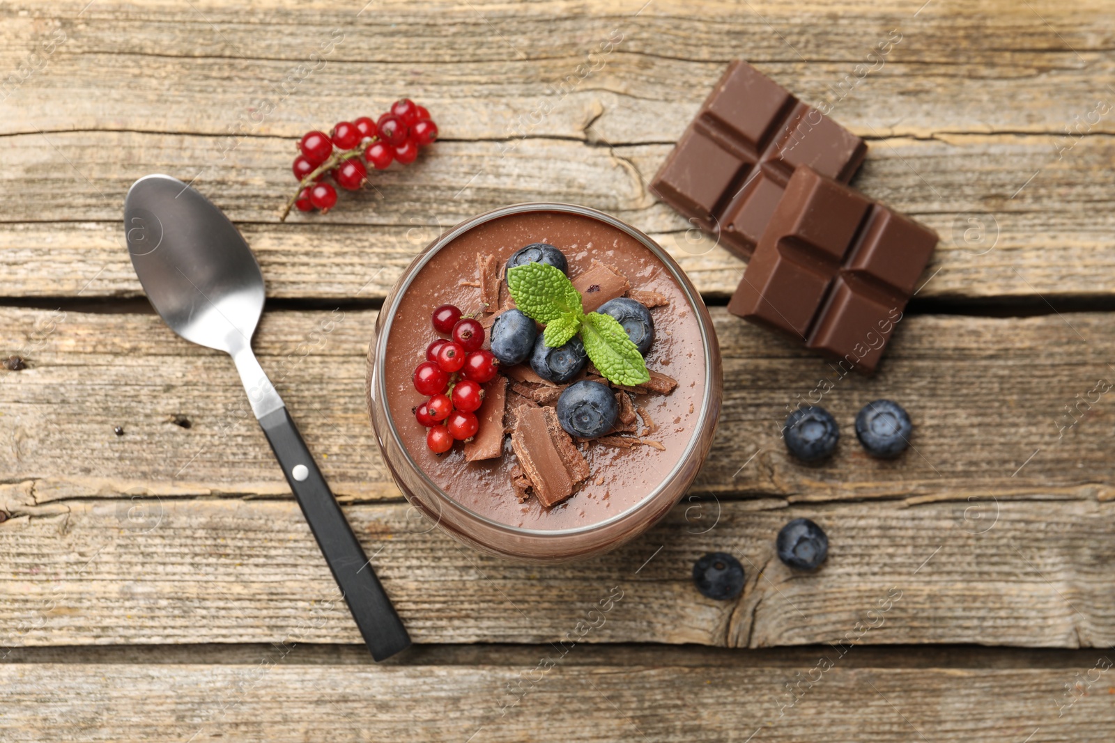 Delicious panna cotta with chocolate, berries, mint and spoon on wooden table, flat lay Photo of Delicious panna cotta with chocolate, berries, mint and spoon on wooden table, flat lay