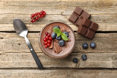 Photo of Delicious panna cotta with chocolate, berries, mint and spoon on wooden table, flat lay