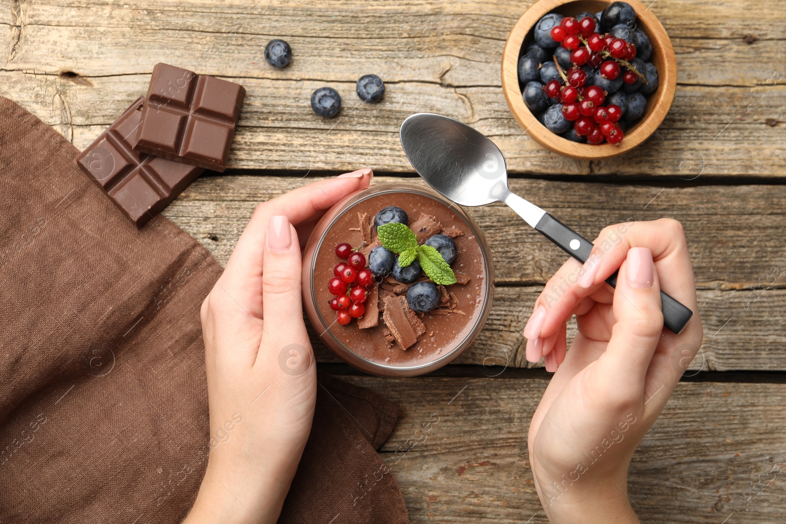 Photo of Woman with delicious chocolate panna cotta and spoon at wooden table, top view