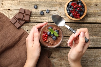 Photo of Woman with delicious chocolate panna cotta and spoon at wooden table, top view