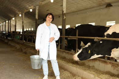 Photo of Farmer with bucket near cute cows inside cowshed in dairy farm