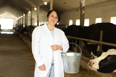 Photo of Portrait of farmer with bucket near cute cows inside cowshed in dairy farm