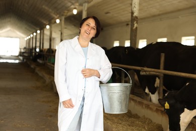 Photo of Portrait of farmer with bucket near cute cows inside cowshed in dairy farm