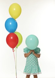 Photo of Little girl in dress hiding behind balloon on white background