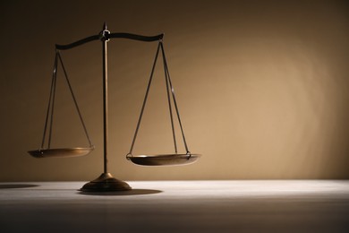 Photo of Scales of justice on table against beige background. Space for text