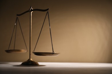 Photo of Scales of justice on table against beige background. Space for text
