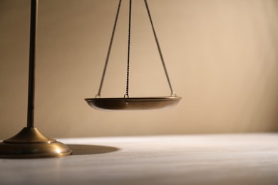 Photo of Scales of justice on table against beige background, closeup