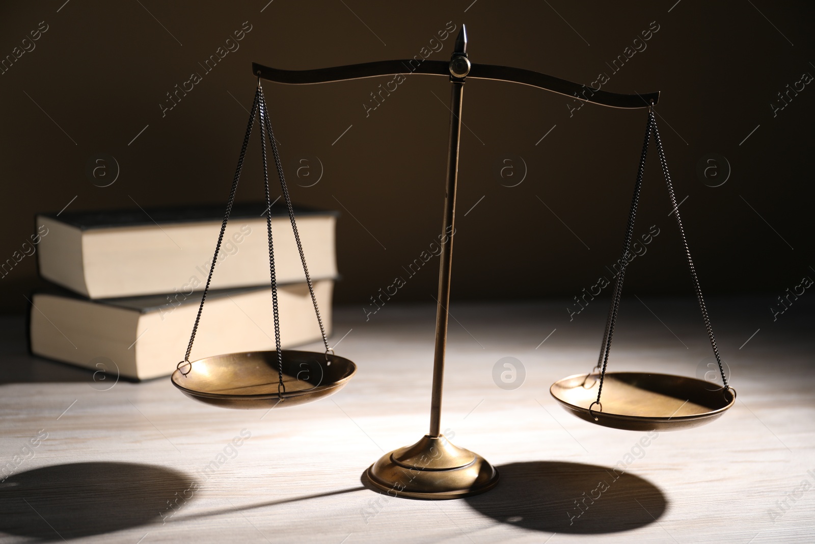 Photo of Scales of justice and books on wooden table against dark background, closeup