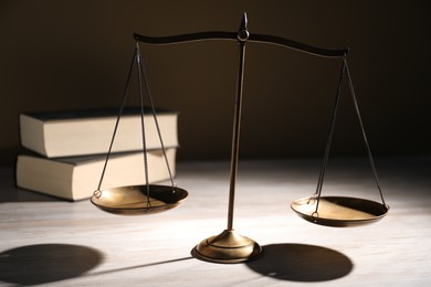 Photo of Scales of justice and books on wooden table against dark background, closeup