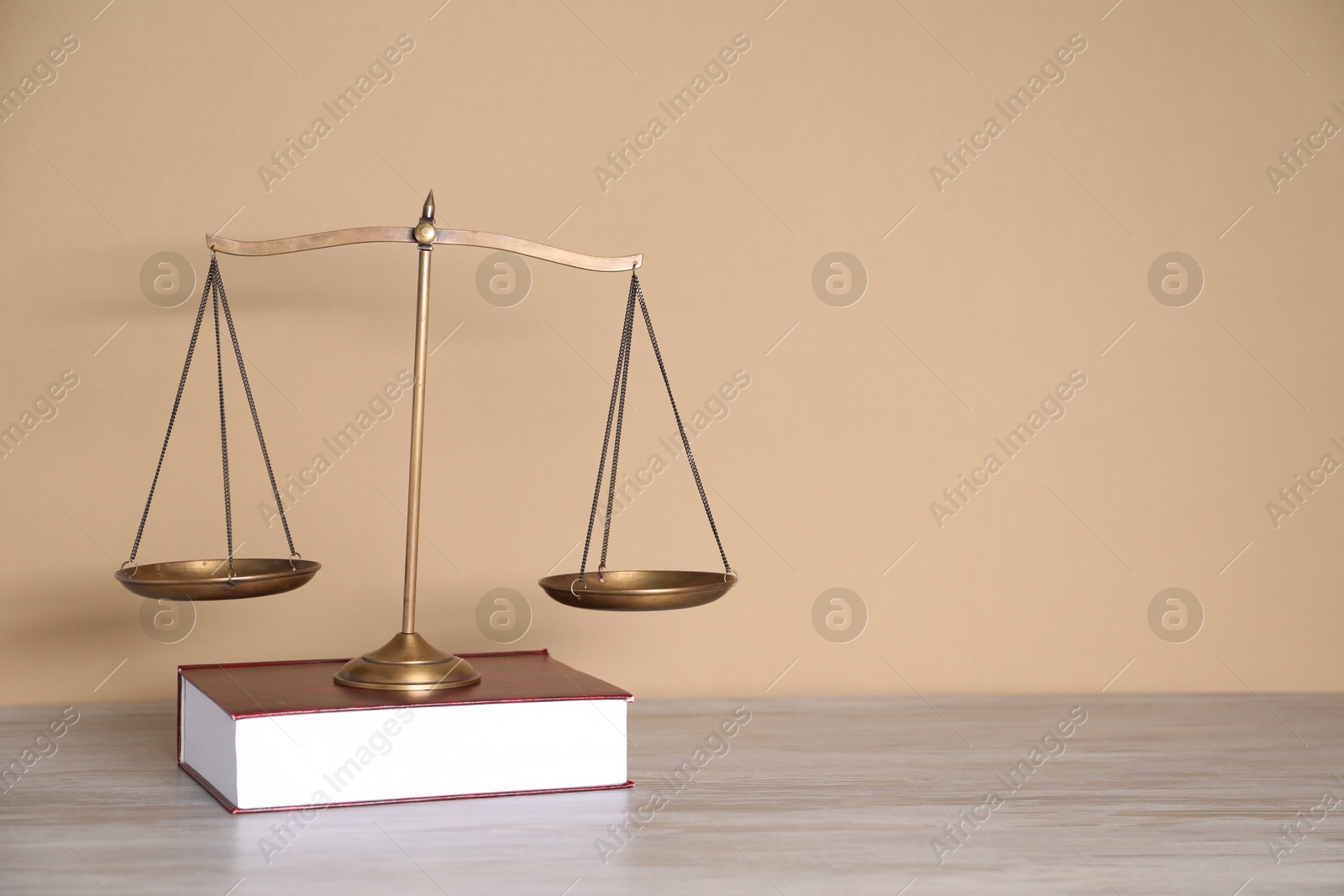 Photo of Scales of justice and book on table against beige background. Space for text