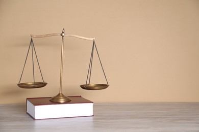Photo of Scales of justice and book on table against beige background. Space for text
