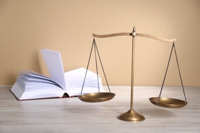 Photo of Scales of justice and book on table against beige background
