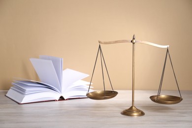 Photo of Scales of justice and book on table against beige background
