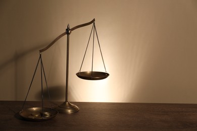 Photo of Scales of justice on wooden table against beige background. Space for text