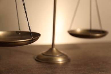 Photo of Scales of justice on wooden table against beige background, closeup