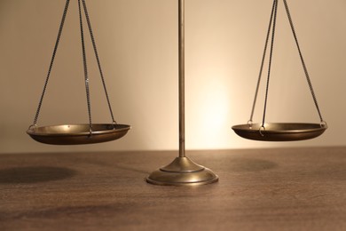 Photo of Scales of justice on wooden table against beige background, closeup