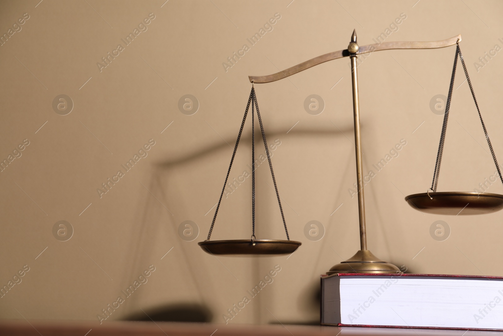 Photo of Scales of justice and book on table against beige background. Space for text