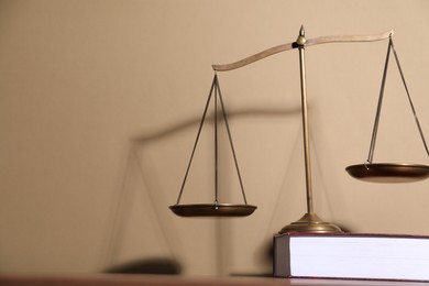 Photo of Scales of justice and book on table against beige background. Space for text