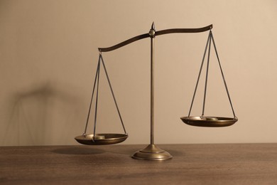 Photo of Scales of justice on wooden table against beige background