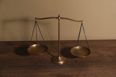 Photo of Scales of justice on wooden table against beige background