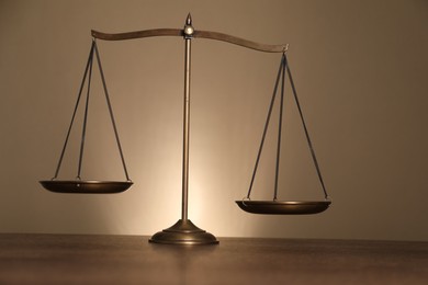 Photo of Scales of justice on wooden table against beige background